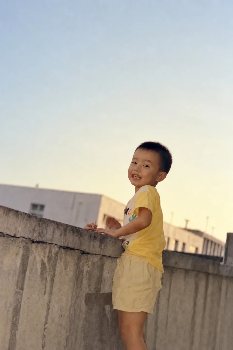 Ricky as a child, wearing yellow beside a wall.