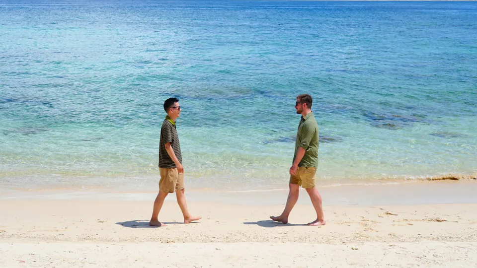 Ricky and Kees facing each other on a beach beside the sea.